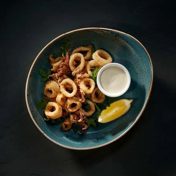 Fried calamari in teal bowl with dipping sauce, lemon, and greens.