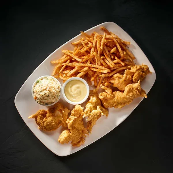 Chicken tenders, french fries, coleslaw, dipping sauce on a white plate.
