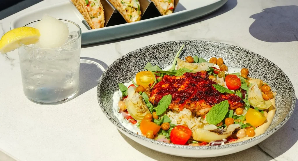 Spiced fish bowl, rice, mixed greens, and a lemon-garnished drink.