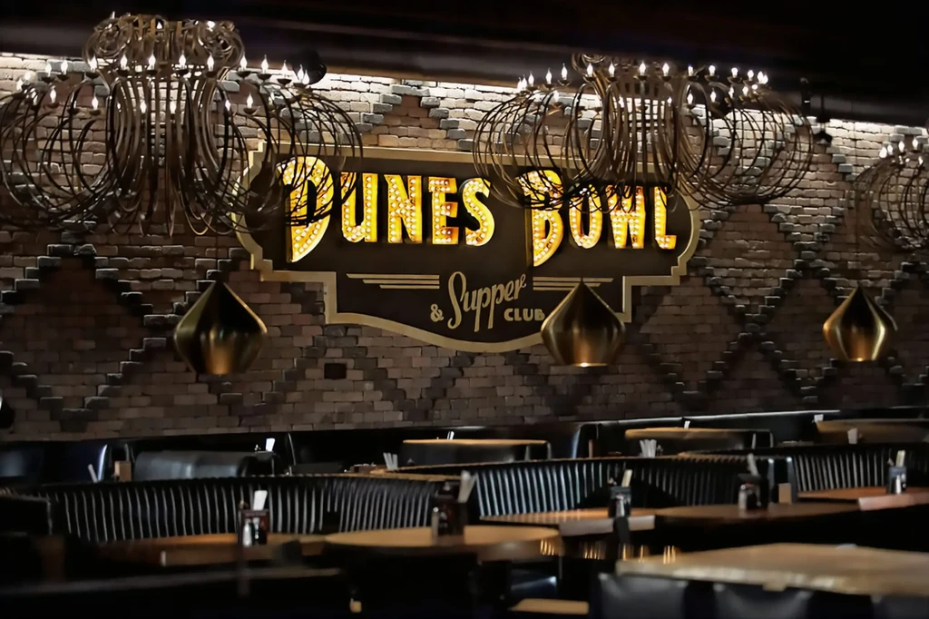 Interior of Dunes Bowl Supper Club with sign, chandeliers, and dim lighting.