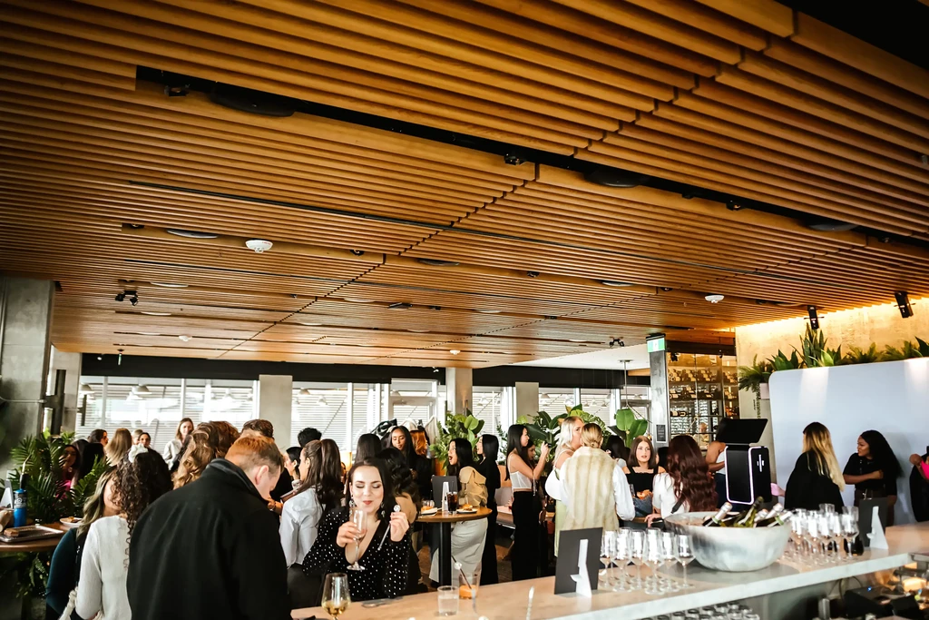 Modern restaurant interior, wooden ceiling, marble bar, people socializing.