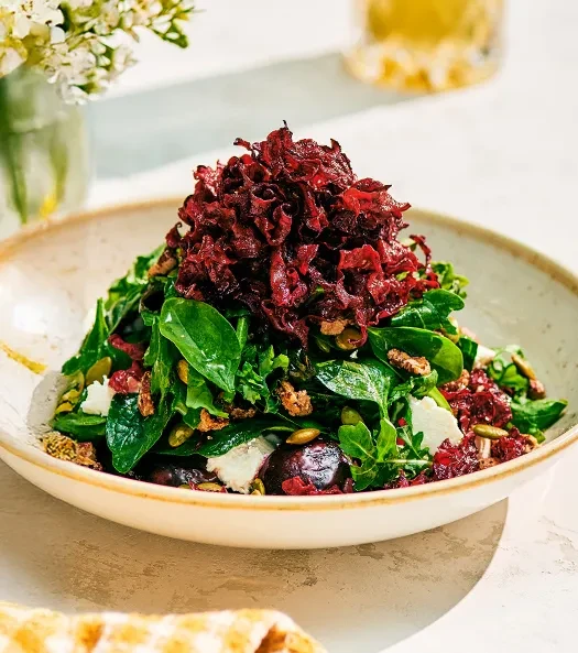 Vibrant salad with green leaves, red topping, cheese, seeds, and nuts.