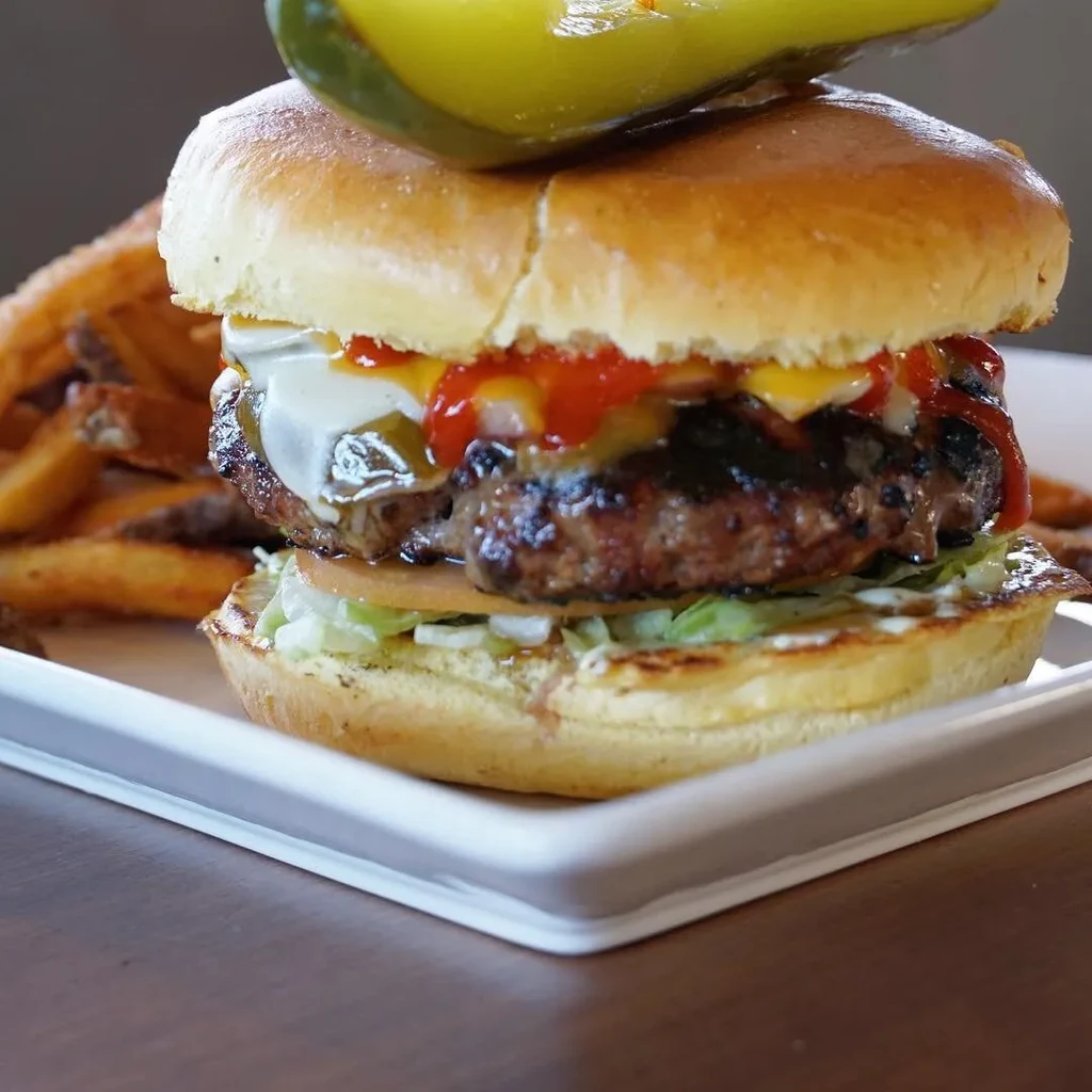 Close-up of a gourmet burger with pickle spear and fries.