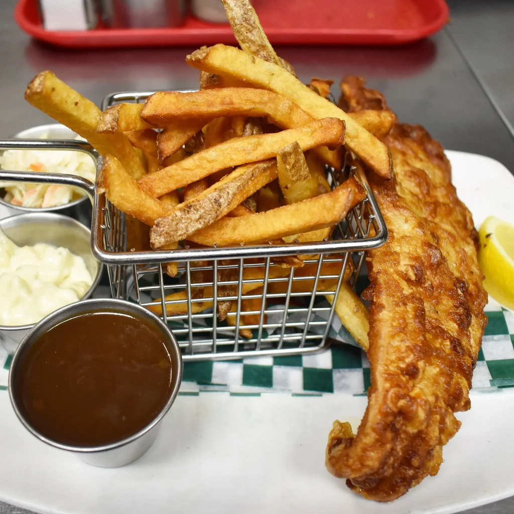 Plate of battered fish, crispy fries, lemon, and various sauces.