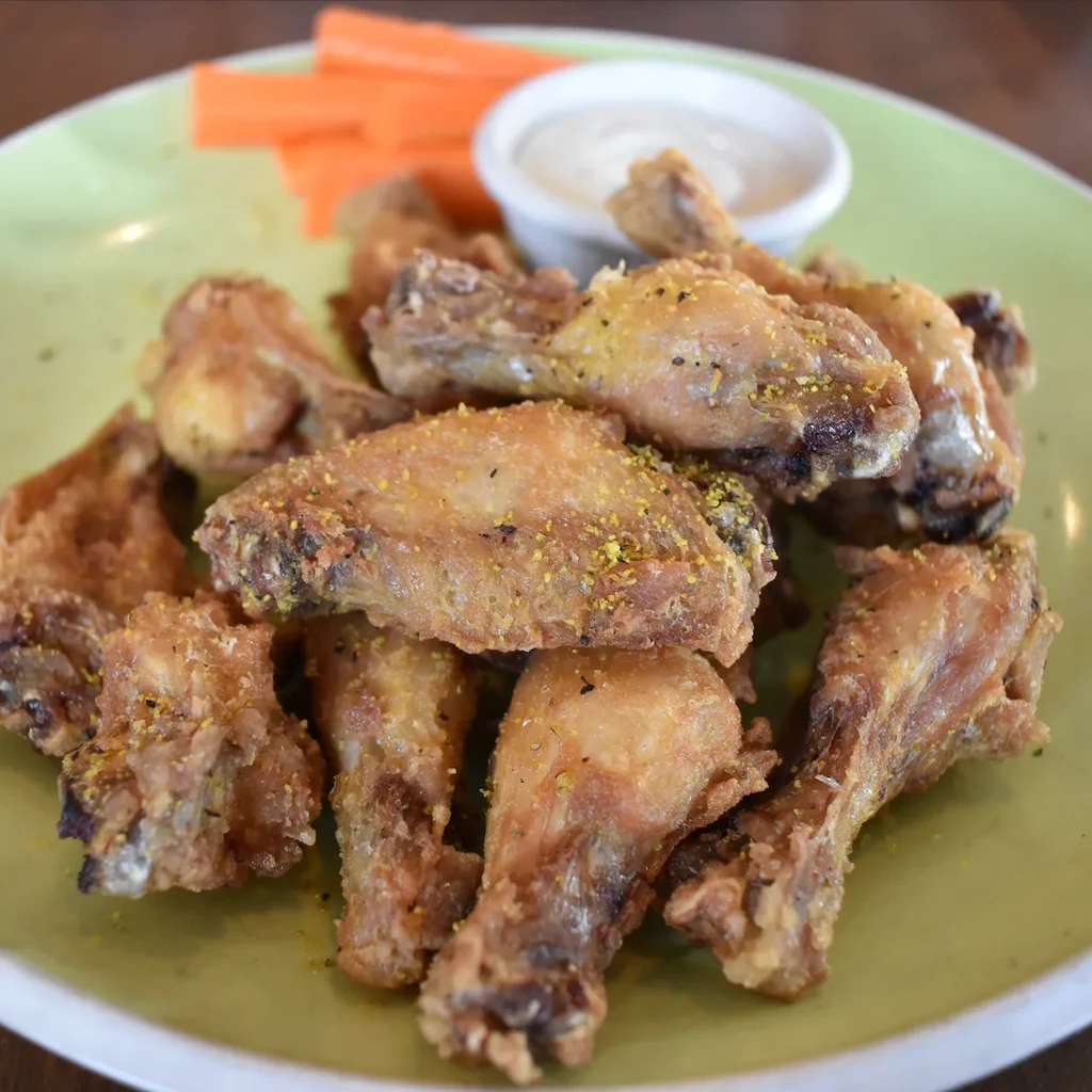 A dozen crispy fried chicken wings with dipping sauce and carrots.