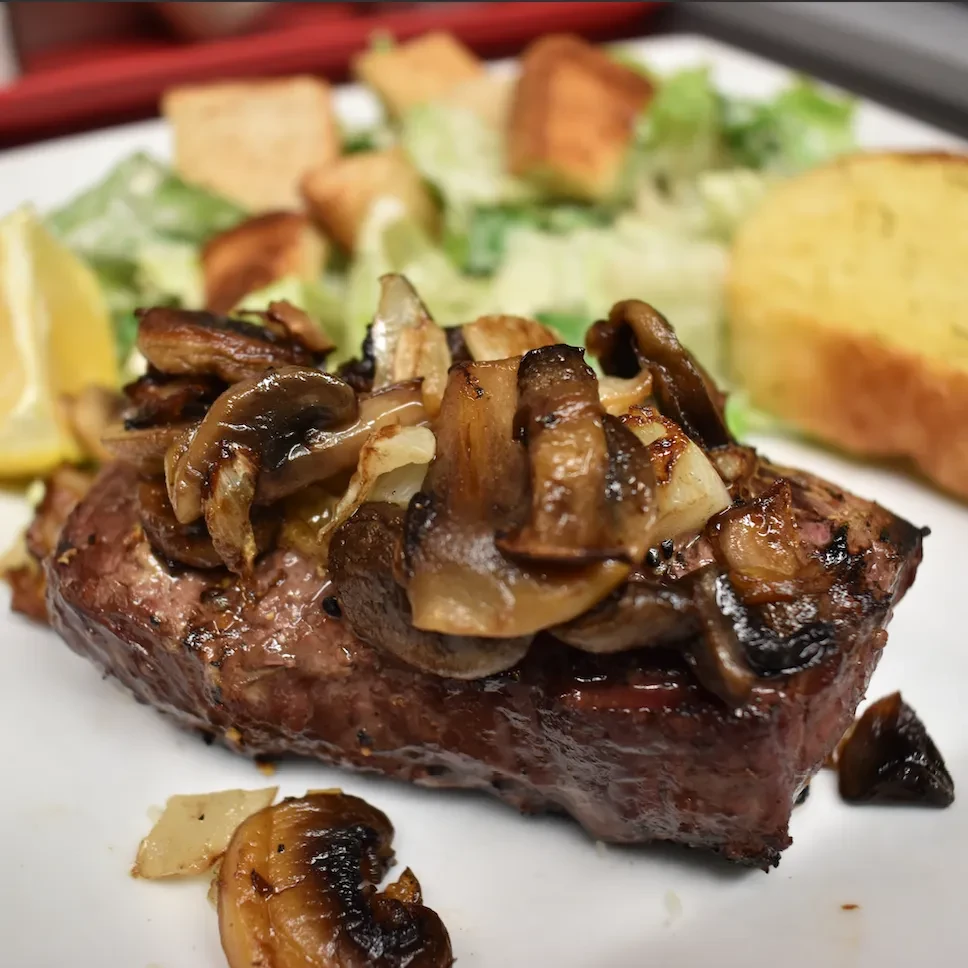 Grilled steak topped with mushrooms, onions, with Caesar salad and bread.