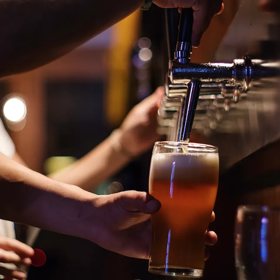 Hands pouring golden beer into a glass from a tap.