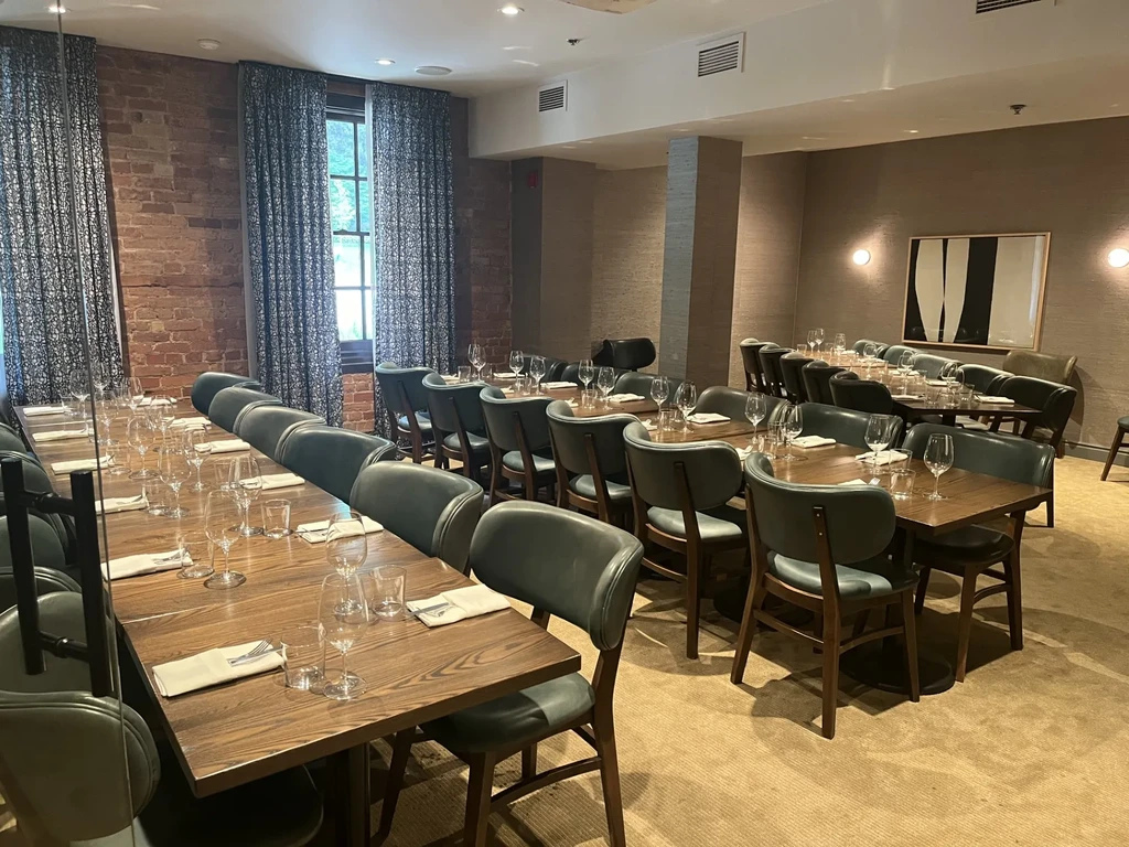 Elegant restaurant dining room with set tables, leather chairs, and brick wall.