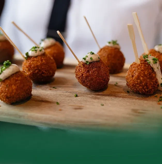 Golden appetizers with sauce, chives, and skewers on a wooden board.