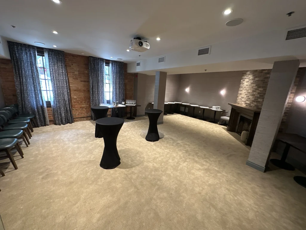 Empty modern event space with high-top tables, brick wall, and buffet.