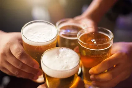 Four foamy golden beers held by multiple hands in a toast.