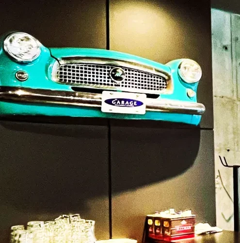 Teal retro car front with "GARAGE" plate mounted on a dark wall.