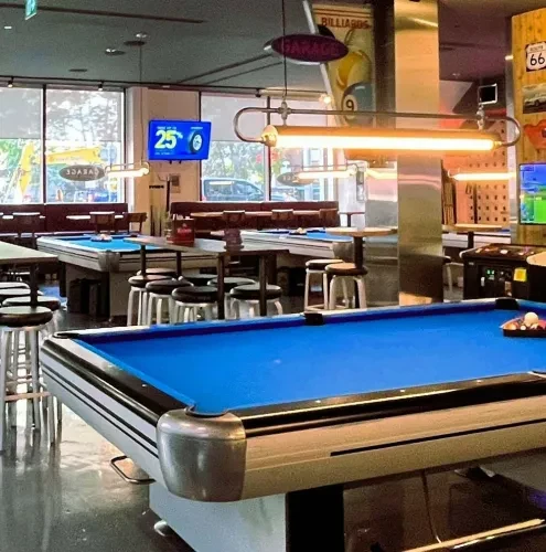 Modern industrial billiards hall with multiple blue-felt pool tables.
