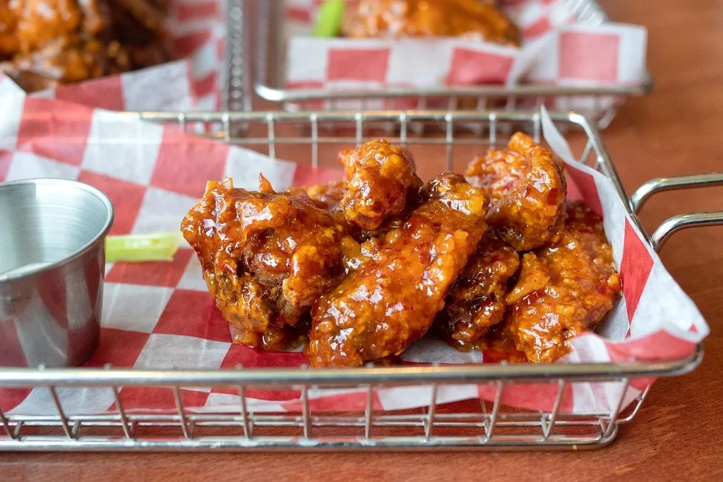 Basket of glistening red-orange chicken wings with celery and dip.