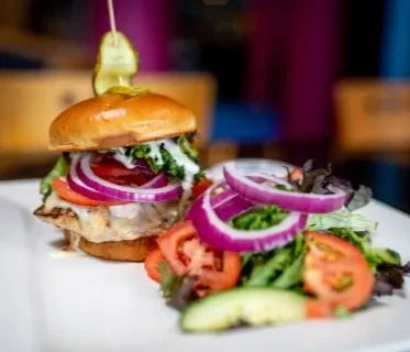Burger on brioche bun with grilled patty, melted cheese, and side salad.