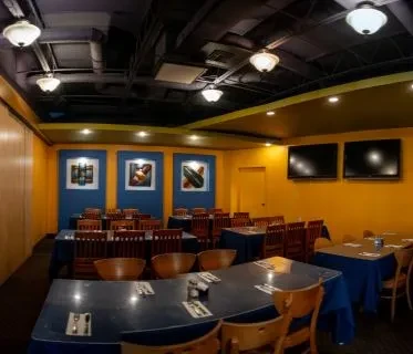 Empty casual restaurant with yellow walls, dark ceiling, and set tables.