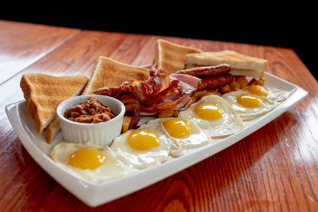 A large breakfast platter with eggs, bacon, sausage, ham, beans, toast.