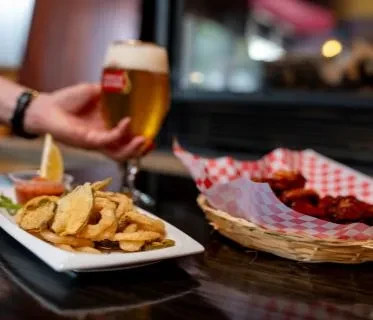 Hand holding Stella Artois beer, fried food, and chicken wings.