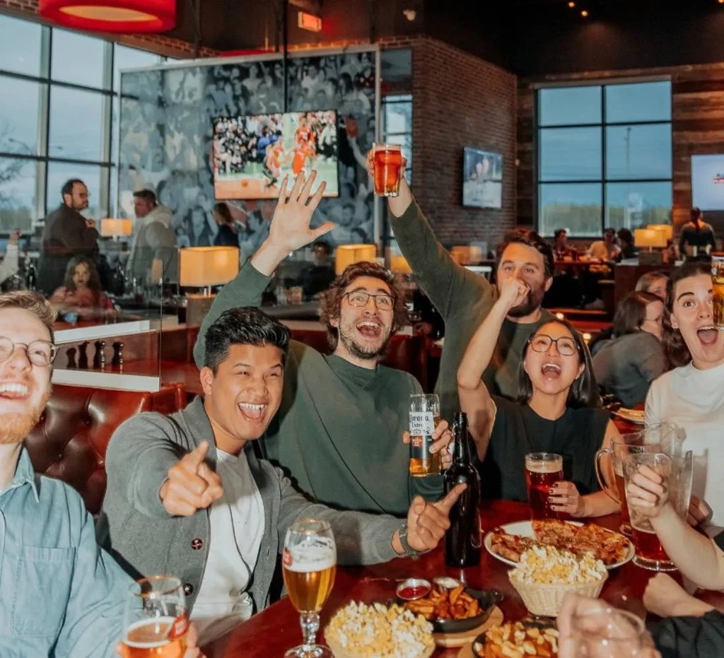 Diverse young adults celebrate with food, beer in a lively sports bar.