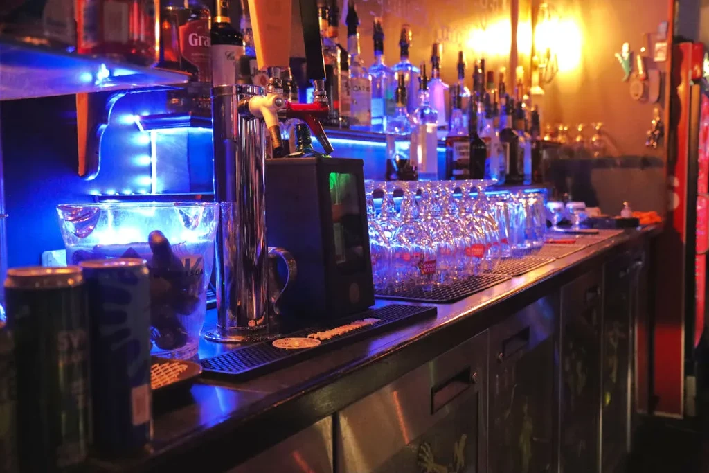 Bar counter with liquor bottles, beer tap, and blue-orange lighting.