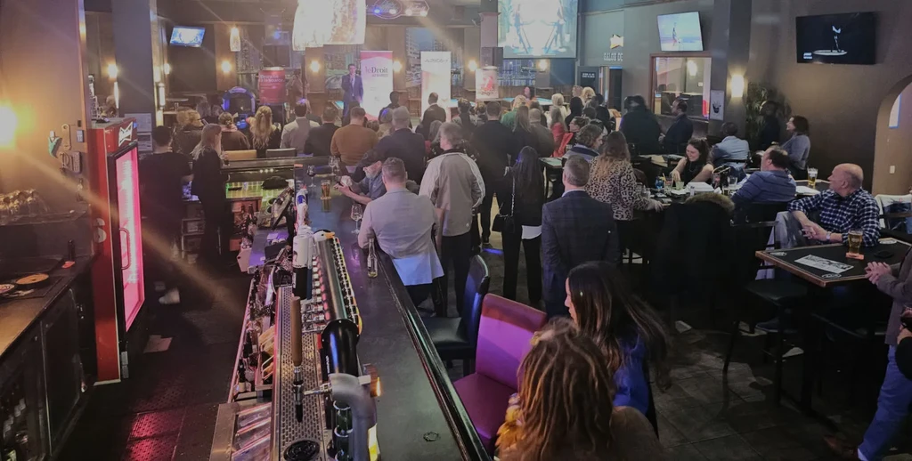 Crowded bar or restaurant event with a speaker on a lit stage.