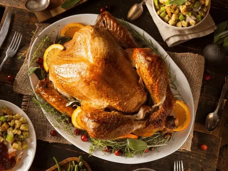 Golden-brown roasted turkey garnished with fruit and herbs, surrounded by side dishes.