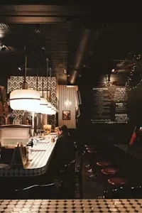 Dimly lit bar interior, curved counter, retro lights, person, checkerboard floor.