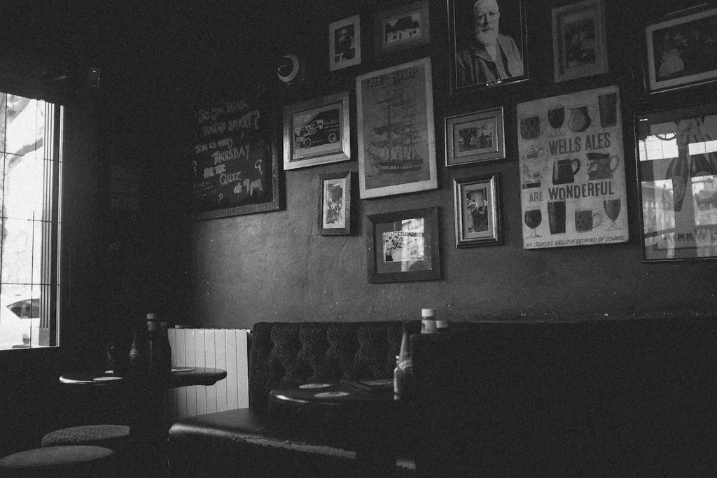 Grainy black and white pub interior with booths, posters, quiz board.