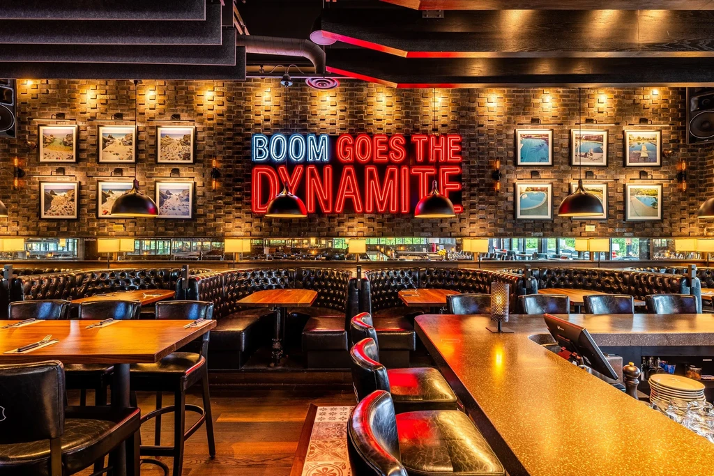 Modern bar interior with dark booths, exposed brick, and a neon sign.