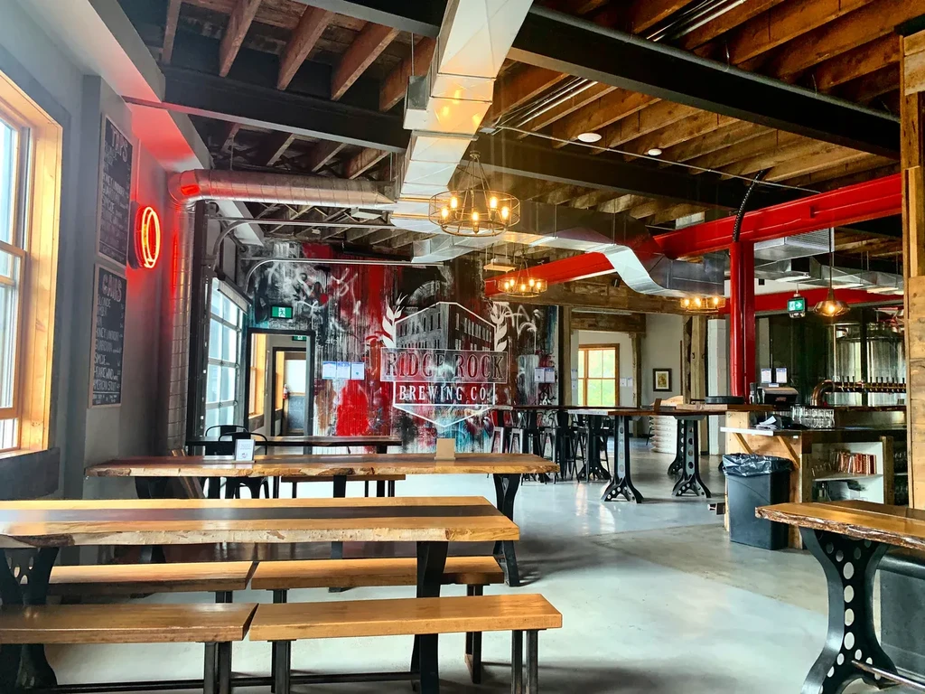 Industrial-chic brewpub interior with exposed beams, picnic tables, and brewery mural.