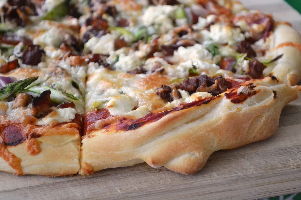 Close-up of rustic pizza with cheese, meat, green vegetables, red onions.