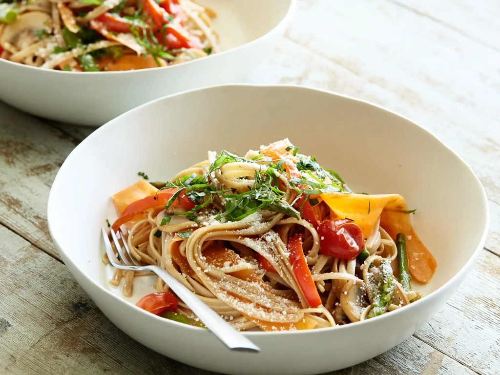 Two bowls of vibrant vegetable pasta with cheese on a wooden table.