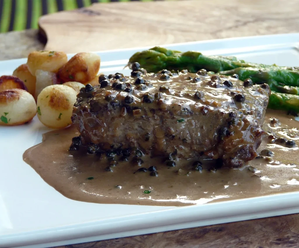 Plated steak with peppercorn sauce, roasted potatoes, and green asparagus.