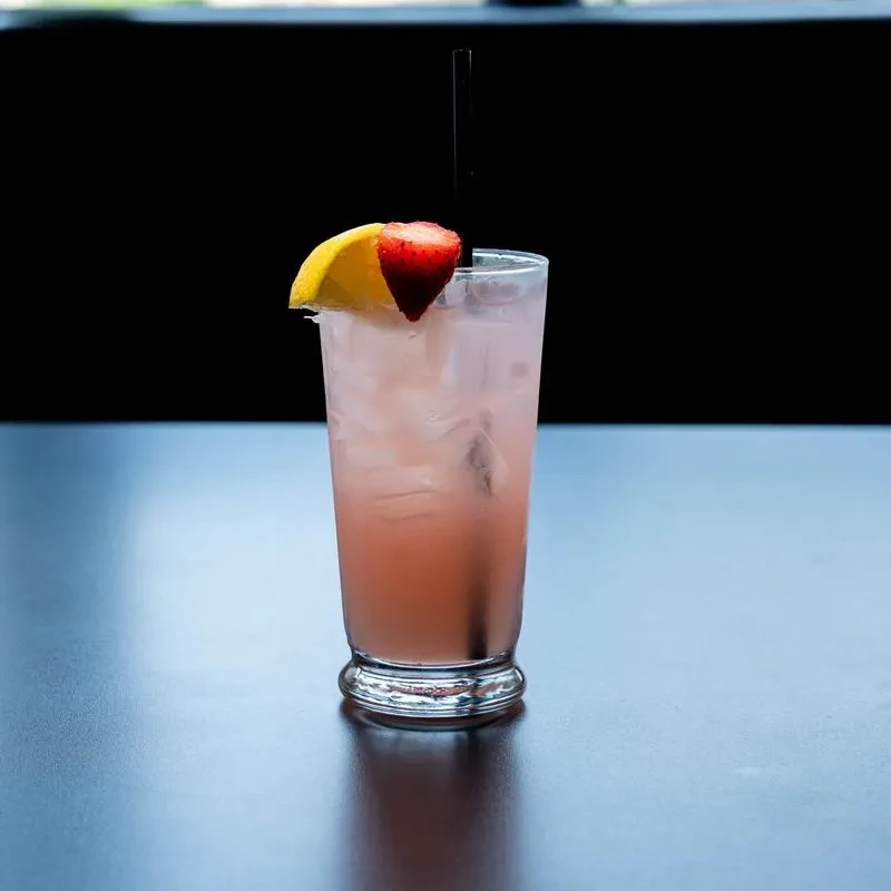Light pink iced drink with straw, lemon, and strawberry garnish.