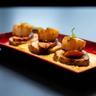 Three seared scallops, foie gras, yellow sauce, and green garnish on red plate.