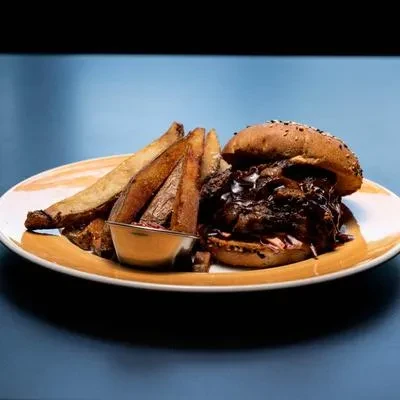 Pulled pork burger with coleslaw, potato wedges, and dipping sauce.