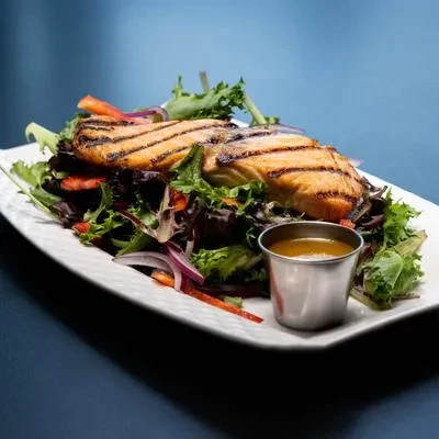 Grilled salmon with char marks, mixed greens, and dressing.
