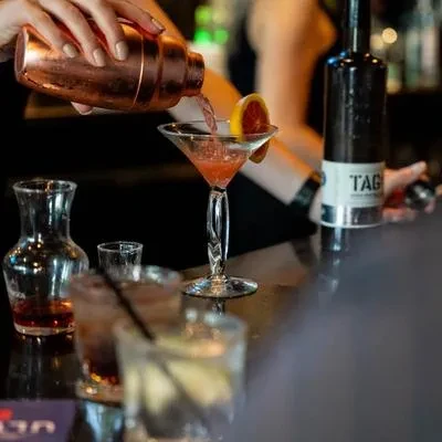 Hands pour red cocktail from copper shaker into garnished martini glass.