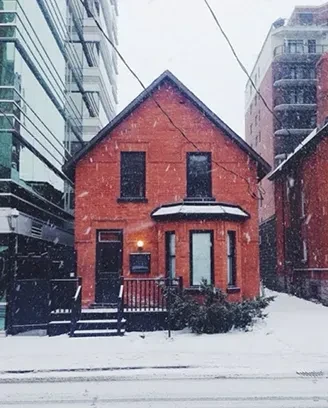 Red brick building in snowy urban landscape, flanked by modern structures.