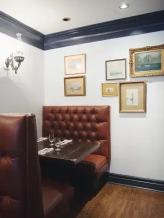 Restaurant corner booth with tufted leather, set table, and framed artwork.
