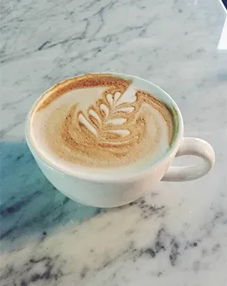 White mug of latte with fern leaf art on marble.