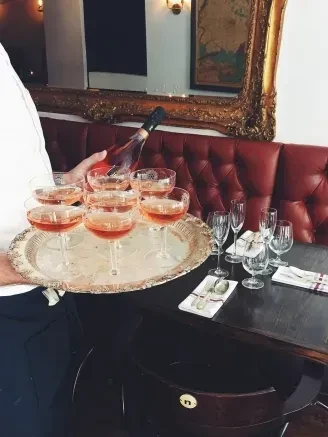 Person pours pink sparkling drinks into coupe glasses on a tray.