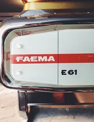 Close-up of FAEMA E61 espresso machine side panel, white with red stripe.