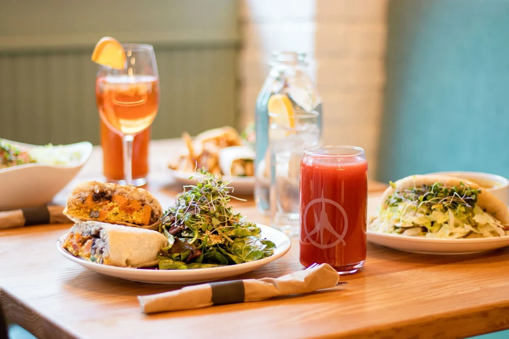 A restaurant table with a burrito, salad, and peace sign drink.