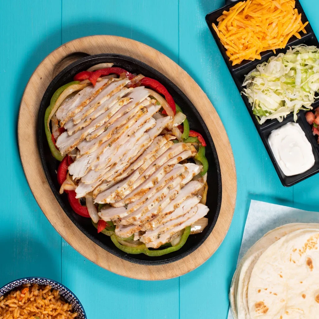 Overhead of a sizzling chicken fajita platter with various accompaniments.