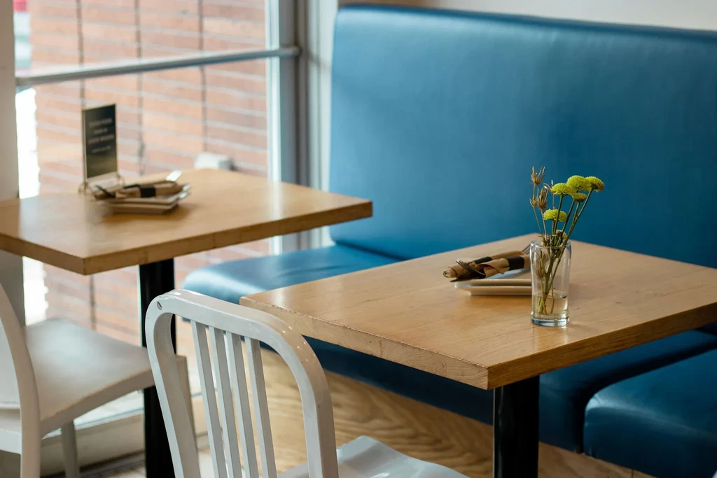 Bright, cozy cafe corner with tables, blue booth, and flowers.