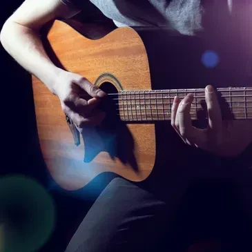 Hands playing an acoustic guitar, highlighted by blue and purple lights.