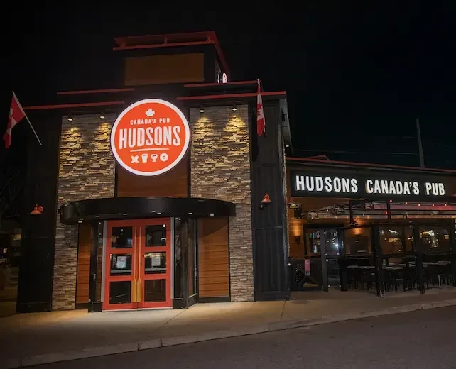 Hudsons Canada's Pub exterior at night, with illuminated sign and patio.