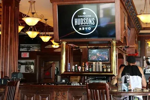 Warmly lit dark wood pub with Hudsons logo and sports on screens.