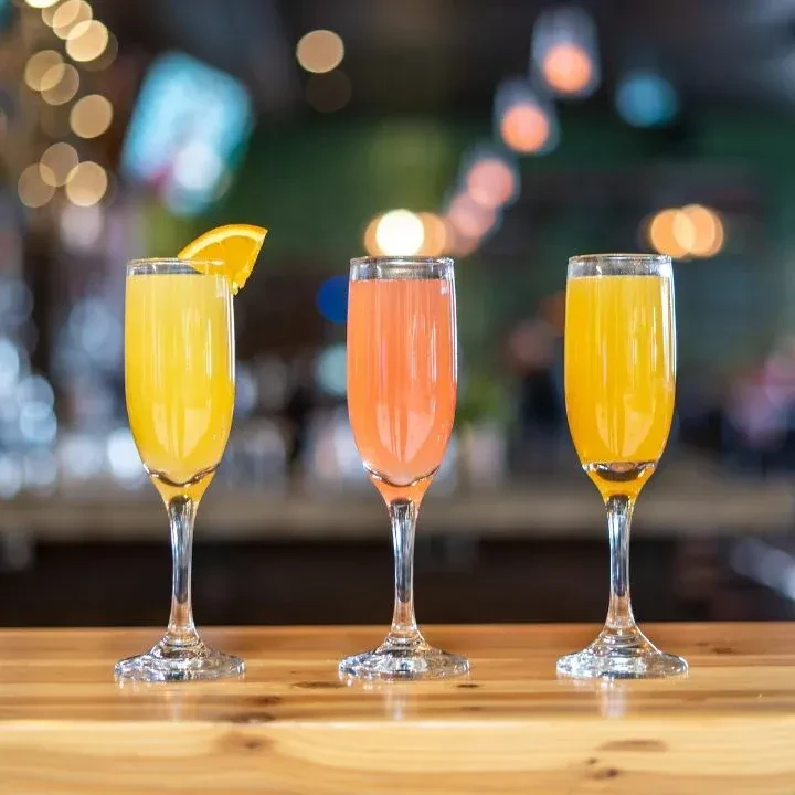 Three champagne flutes, yellow and pink drinks, one garnished, on a bar.